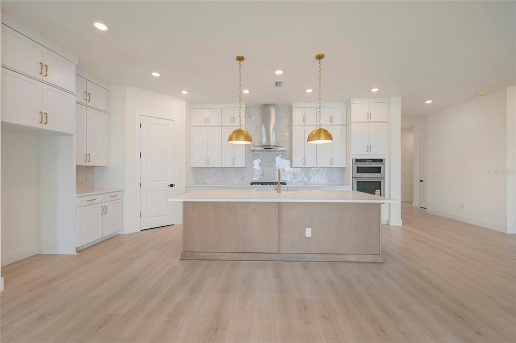 A modern kitchen features white cabinetry, a light wood island, and gold pendant lights — 17988 FOXTAIL LOOP, VENICE, FL