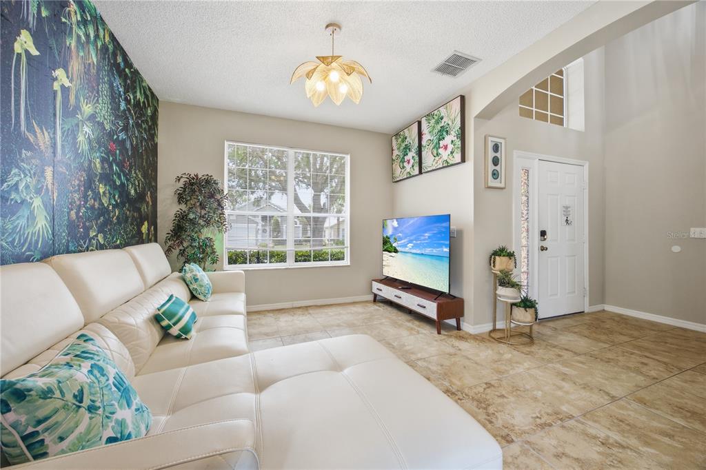 A living room features a white sectional sofa, tiled floors, a television, and tropical wallpaper — 2658 EMERALD ISLAND BOULEVARD, KISSIMMEE, FL