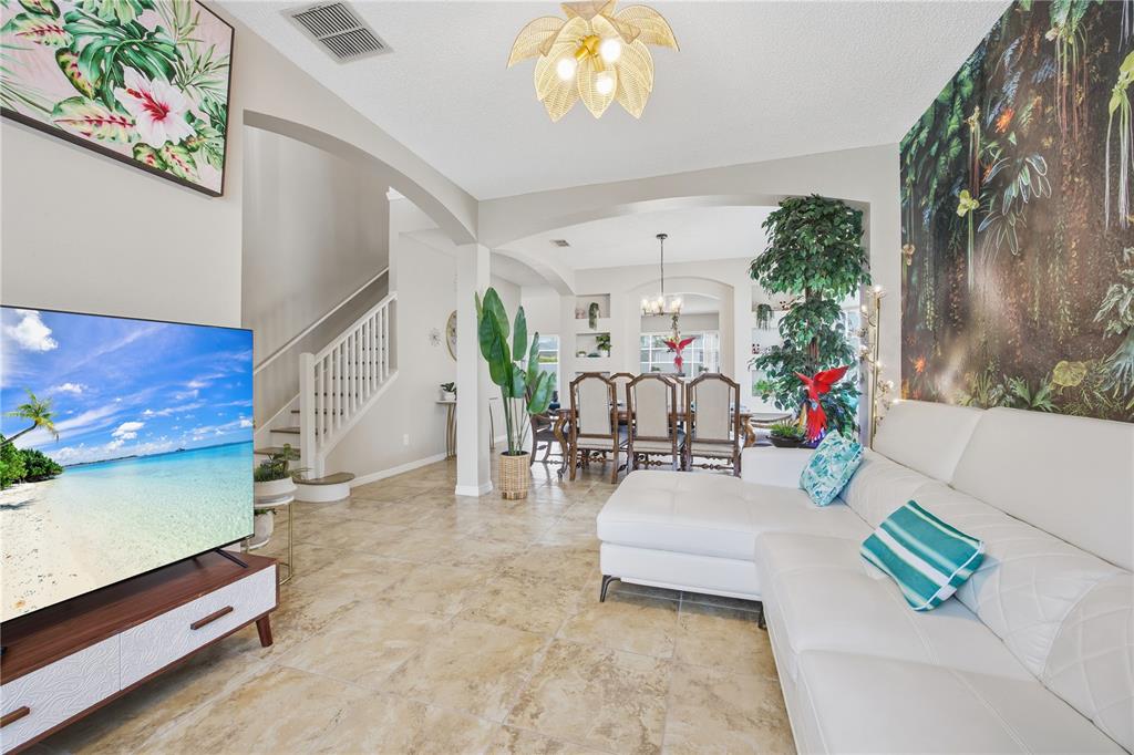 A living room with a white sectional sofa, tile floors, and a large tropical wall mural — 2658 EMERALD ISLAND BOULEVARD, KISSIMMEE, FL