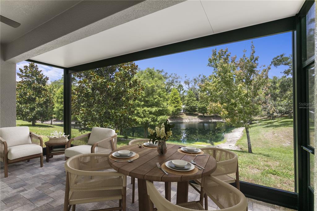 A screened-in patio with paver flooring overlooks a grassy yard and a small pond — 602 OZONA VILLAGE DRIVE, PALM HARBOR, FL