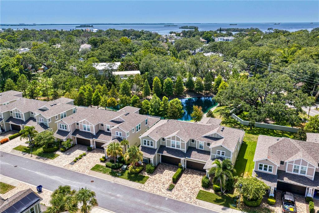 An aerial view shows a residential neighborhood with houses, a small pond, and a nearby bay — 602 OZONA VILLAGE DRIVE, PALM HARBOR, FL