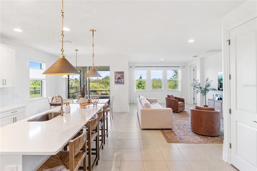An open-concept kitchen and living area with a large island, tile floors, and patio views — 16743 SERAPHIC TRAIL, BRADENTON, FL