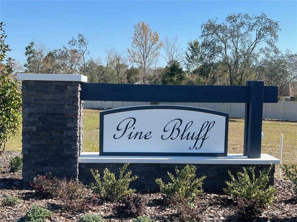 A stone and dark wood monument sign displays the name Pine Bluff in a neighborhood — 12508 LANGLEY DRIVE Lot 88, SPRING HILL, FL