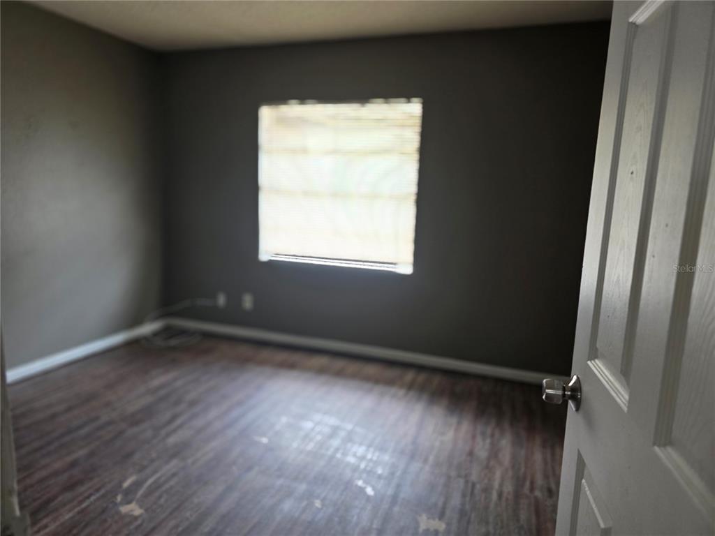 An empty bedroom features dark gray walls, wood-look flooring, and a single window with blinds — 3413 E 12TH AVENUE UNIT A, TAMPA, FL