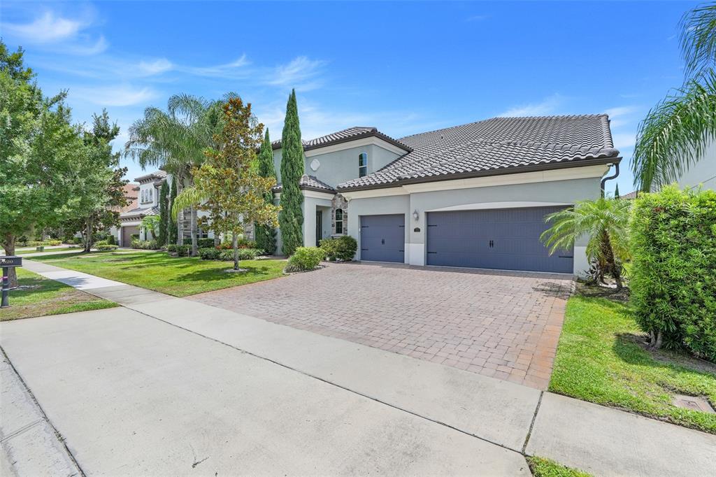 A two-story house with a tile roof, gray garage doors, and a brick paver driveway — 7920 CHILTON DRIVE, ORLANDO, FL