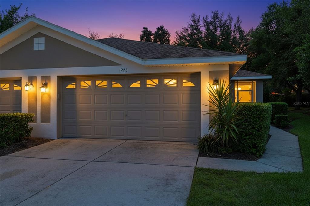 A tan house exterior features a two-car garage, a concrete driveway, and manicured green landscaping — 4228 SILVER STAR DRIVE, SPRING HILL, FL