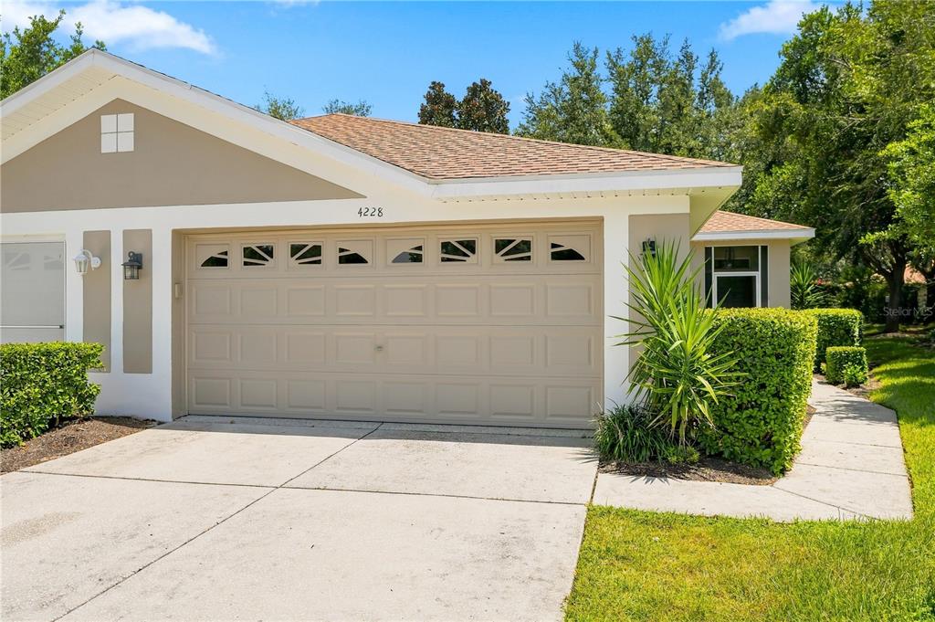 A tan house exterior features a two-car garage, a concrete driveway, and manicured green landscaping — 4228 SILVER STAR DRIVE, SPRING HILL, FL