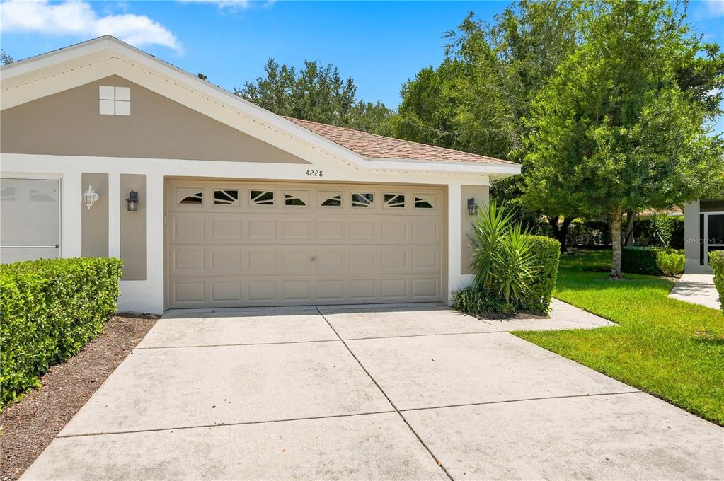A beige house exterior features a two-car garage, a concrete driveway, and manicured landscaping — 4228 SILVER STAR DRIVE, SPRING HILL, FL