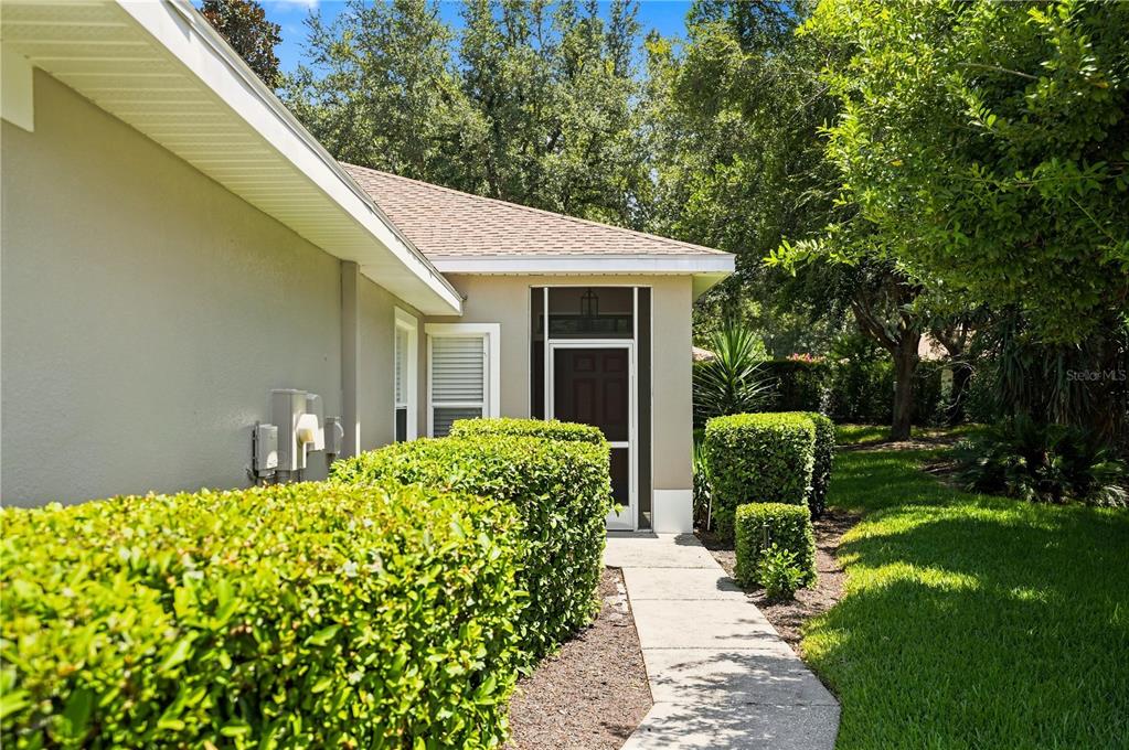 A concrete walkway leads to a screened-in entryway beside a house with manicured hedges — 4228 SILVER STAR DRIVE, SPRING HILL, FL