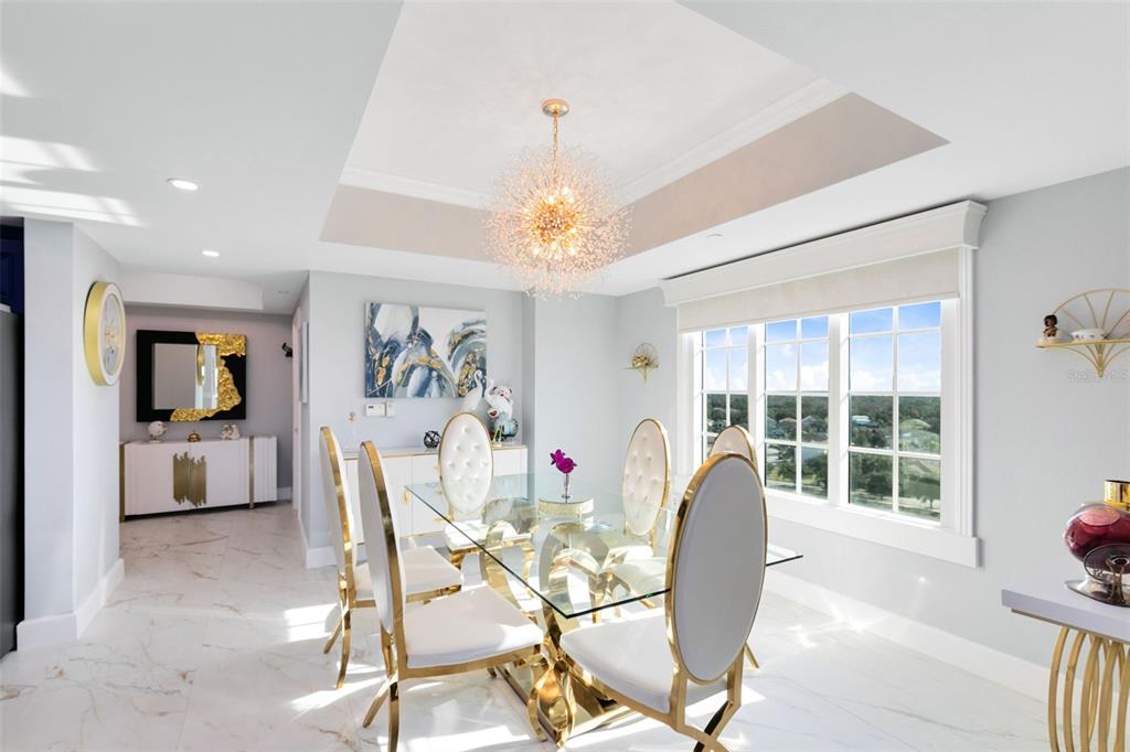 A dining room features a glass table, gold-framed chairs, a chandelier, and marble-look flooring — 7593 GATHERING DRIVE UNIT 802, REUNION, FL