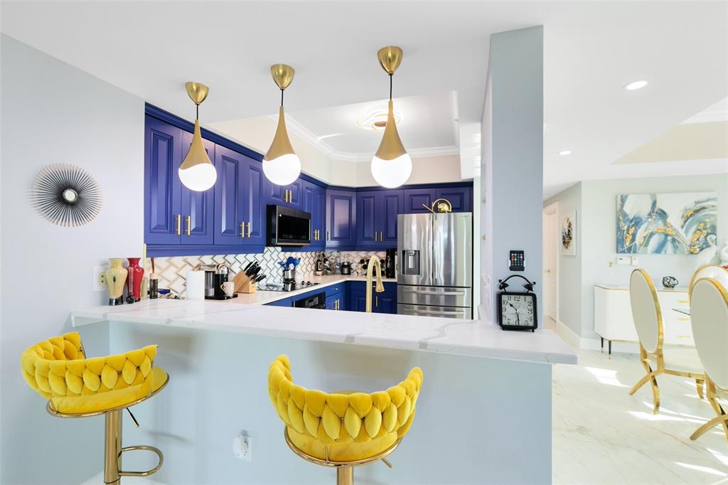 A kitchen features blue cabinets, a white countertop, and two yellow velvet bar stools — 7593 GATHERING DRIVE UNIT 802, REUNION, FL
