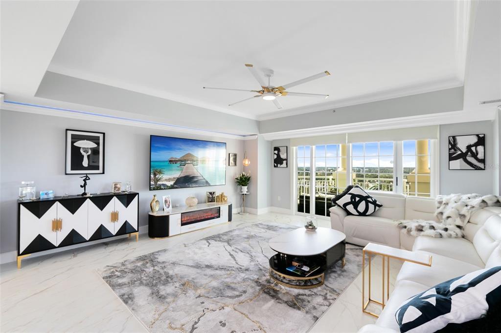 A modern living room features a large area rug, white leather sofa, and a wall-mounted television — 7593 GATHERING DRIVE UNIT 802, REUNION, FL