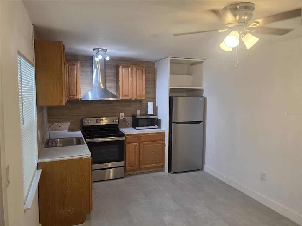 A kitchen features wood cabinets, stainless steel appliances, a tile backsplash, and gray floor tiles — 1844 JOHN RIVERS STREET UNIT N, SARASOTA, FL
