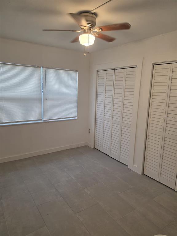 A bedroom with white walls, gray tile flooring, a ceiling fan, and louvered closet doors — 1844 JOHN RIVERS STREET UNIT N, SARASOTA, FL