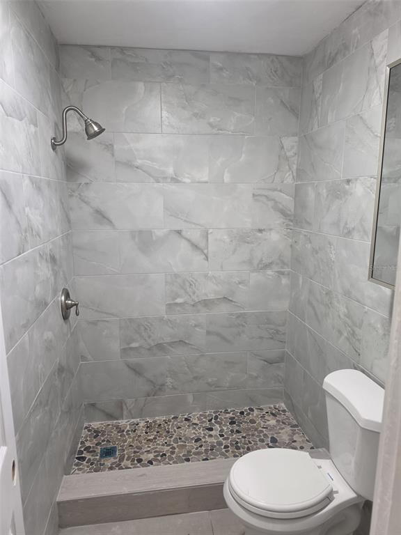 A bathroom featuring a walk-in shower with pebble flooring, gray tile walls, and a toilet — 1844 JOHN RIVERS STREET UNIT N, SARASOTA, FL