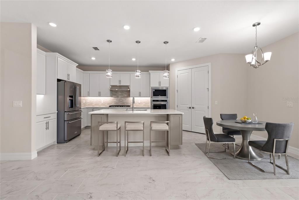 A modern kitchen features white cabinetry, a central island with bar seating, and a dining area — 5173 FOOTHILLS PRESERVE LOOP, MOUNT DORA, FL