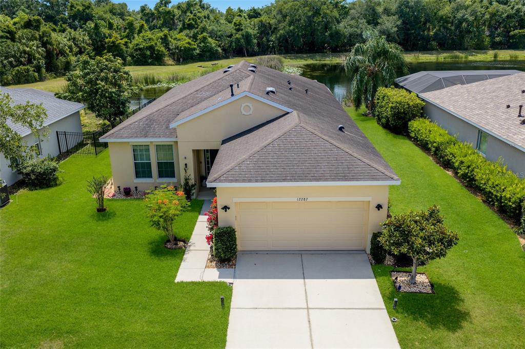An aerial view shows three suburban houses with pools situated along a pond and forest — 12287 LAVENDER LOOP, BRADENTON, FL