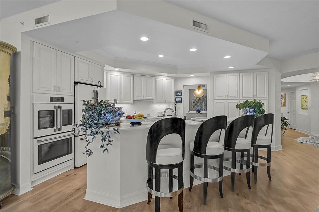 A white kitchen features a breakfast bar with four black stools and light wood flooring — 385 N POINT ROAD UNIT 304, OSPREY, FL