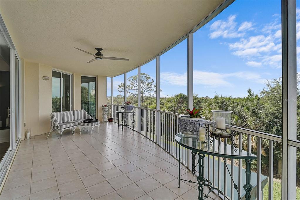A screened-in balcony features tiled flooring, a ceiling fan, and a view of trees — 385 N POINT ROAD UNIT 304, OSPREY, FL