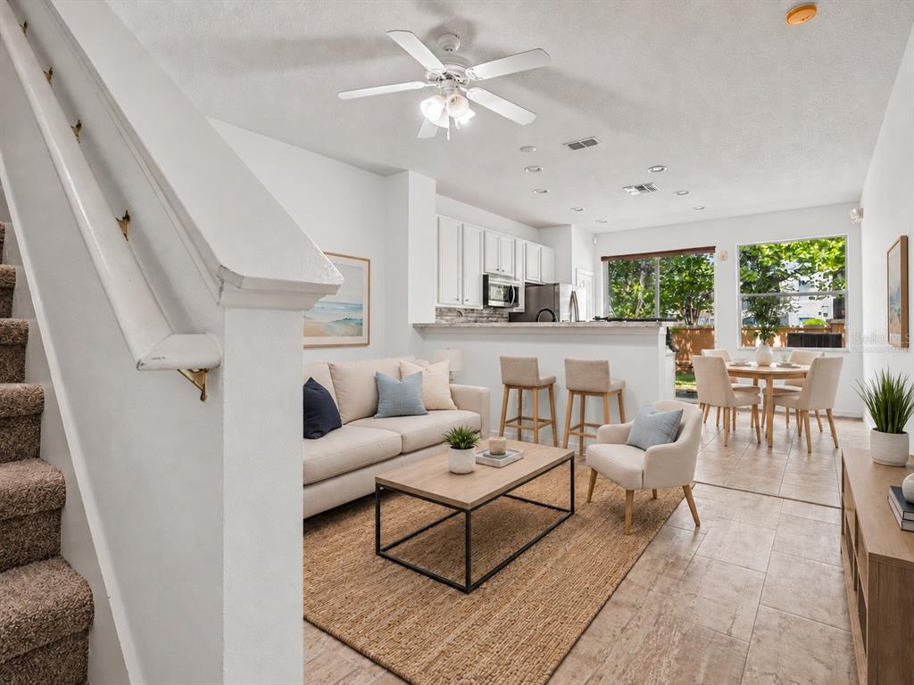 A light blue living area with wood-look tile flooring leads to a kitchen and patio — 7631 LONG ISLAND DR, KISSIMMEE, FL