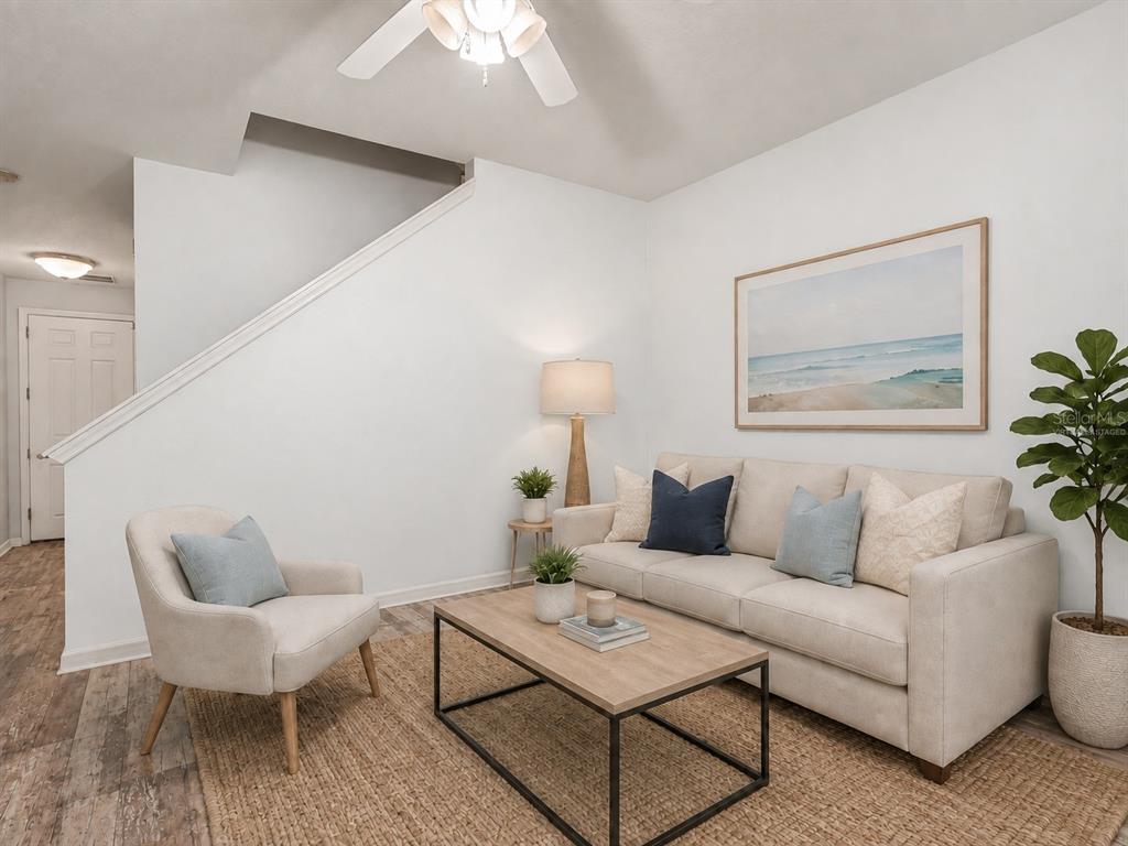 A living area with light blue walls, wood-look flooring, and a staircase leads to a kitchen — 7631 LONG ISLAND DR, KISSIMMEE, FL