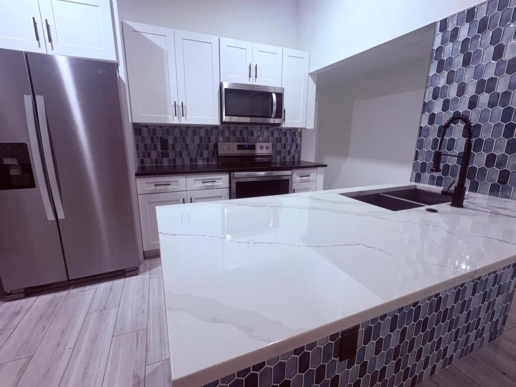 A kitchen features white cabinets, stainless steel appliances, a white quartz island, and blue tile — 885 CARNATION DRIVE, WINTER PARK, FL