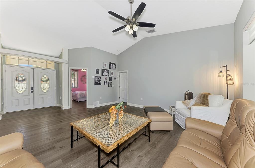A living room features vaulted ceilings, wood-look flooring, a ceiling fan, and tan leather furniture — 583 PINE RANCH EAST ROAD, OSPREY, FL