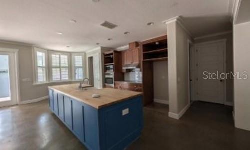 A kitchen features a blue island with a wood countertop, wood cabinetry, and concrete floors — 3355 SCHOOLHOUSE ROAD, HARMONY, FL