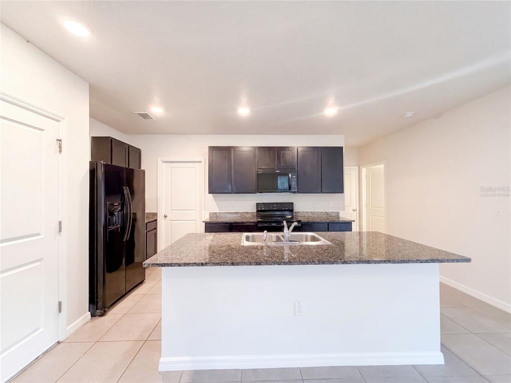 A kitchen features dark cabinetry, granite countertops, a central island with a sink, and appliances — 16805 TRITE BEND STREET, WIMAUMA, FL