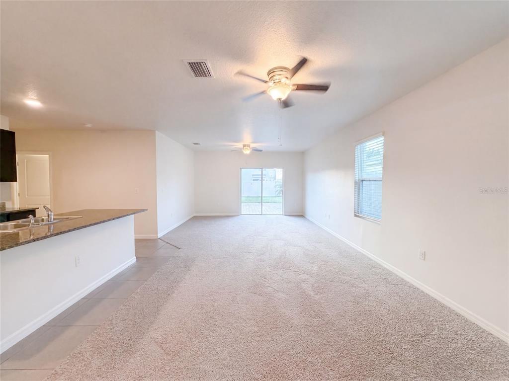 An open-concept living area features beige carpeting, a ceiling fan, and a sliding glass door — 16805 TRITE BEND STREET, WIMAUMA, FL
