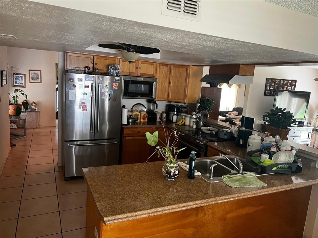 A kitchen features wood cabinets, stainless steel appliances, a granite countertop island, and tile flooring — 7804 SNOWBERRY CIRCLE, ORLANDO, FL