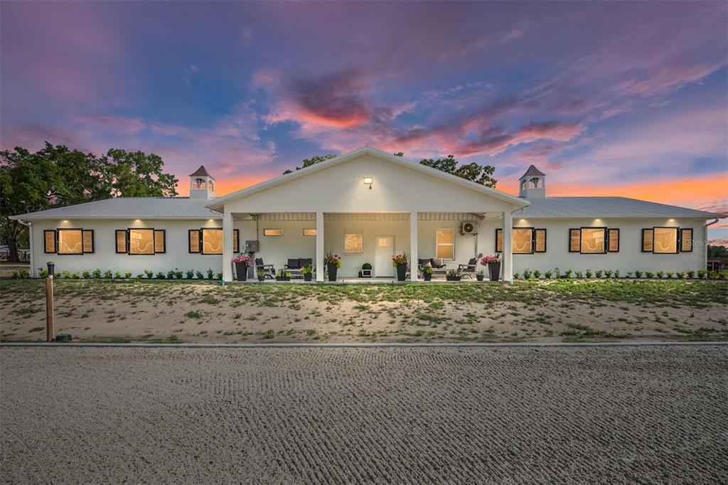 A wide, single-story white house with a covered porch and two cupolas at sunset — 663 NW 80TH AVENUE, OCALA, FL