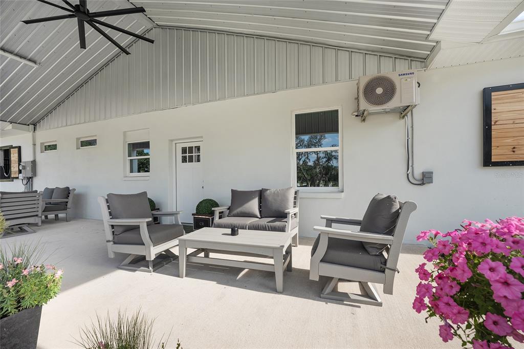 A covered patio features gray outdoor furniture, a white wall, and a mounted air conditioner — 663 NW 80TH AVENUE, OCALA, FL