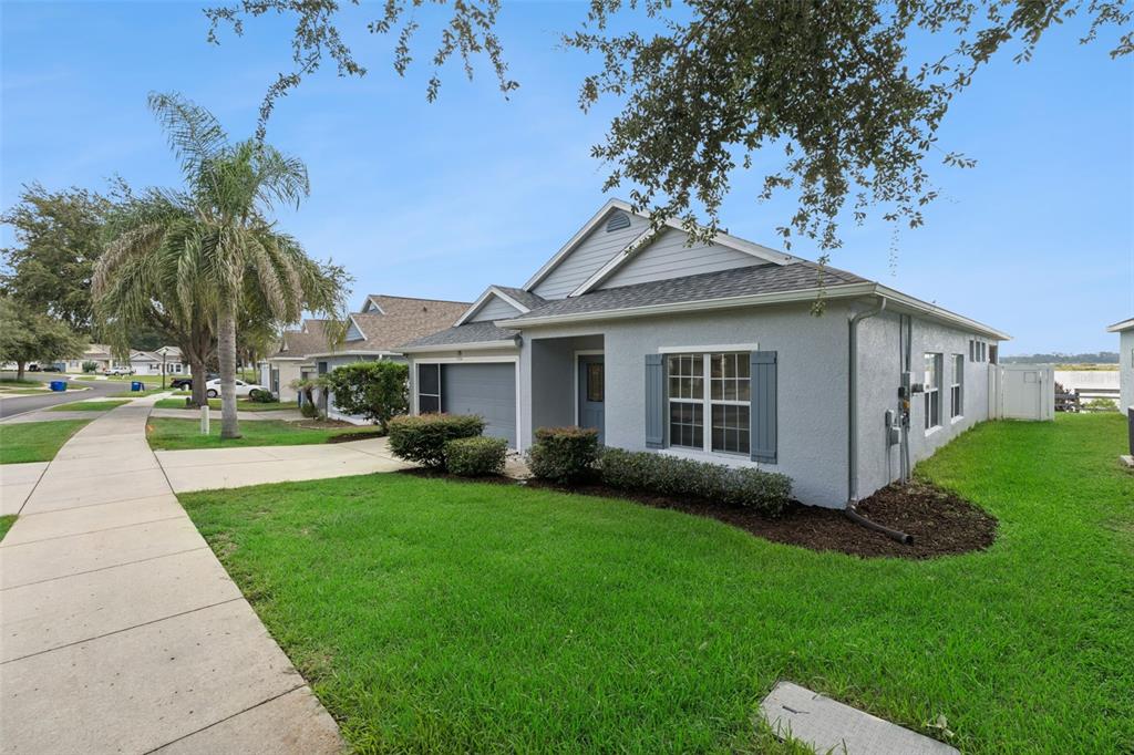 A single-story gray house with a garage, front lawn, and sidewalk under a blue sky — 1324 KELLOGG DRIVE, TAVARES, FL