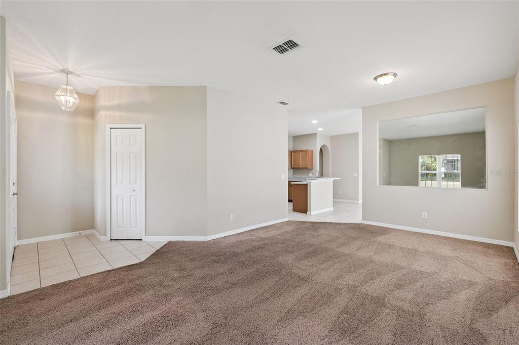A carpeted living room features a tiled entryway, a white door, and a large wall cutout — 1324 KELLOGG DRIVE, TAVARES, FL