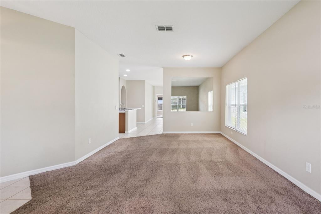 A carpeted living room with beige walls, a large wall cutout, and an adjacent kitchen — 1324 KELLOGG DRIVE, TAVARES, FL