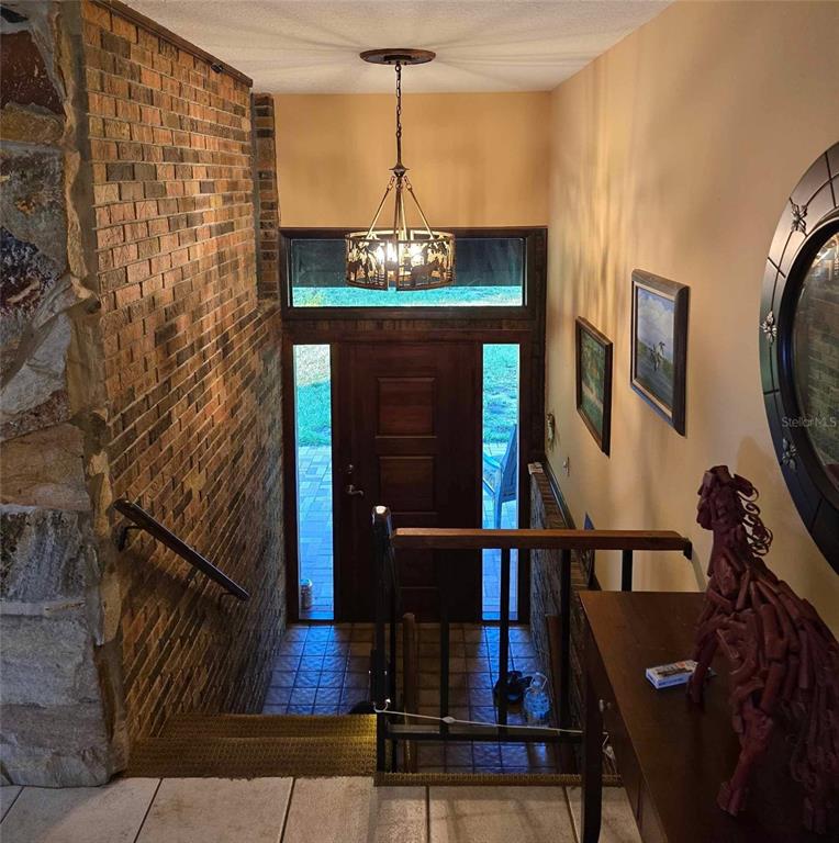 An entryway features a brick wall, a wooden door with sidelights, and a rustic chandelier — 5757 TRASK ROAD, FORT MEADE, FL
