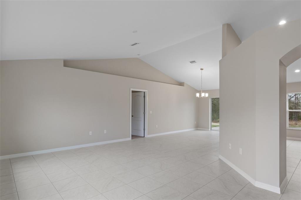 An empty room with light-colored tile flooring, beige walls, and a vaulted ceiling — 12073 MANASSAS AVENUE, WEEKI WACHEE, FL