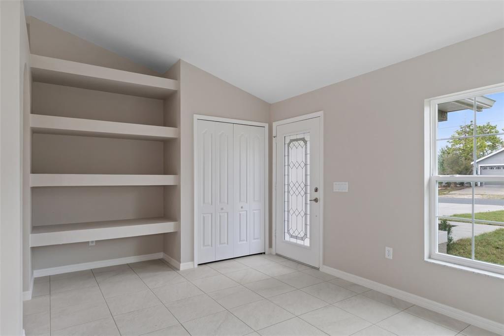 An entryway features light tile flooring, built-in wall shelves, a white closet, and a glass-paneled door — 12073 MANASSAS AVENUE, WEEKI WACHEE, FL