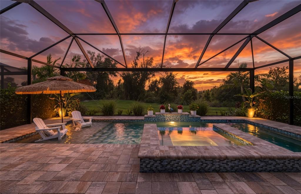 A screened-in pool and spa area with a sunset view over a grassy landscape — 5119 CASERTA COURT, PALMETTO, FL