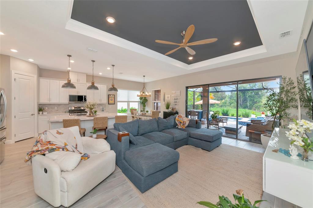 An open-concept living room and kitchen feature a tray ceiling, blue sectional, and sliding doors — 5119 CASERTA COURT, PALMETTO, FL