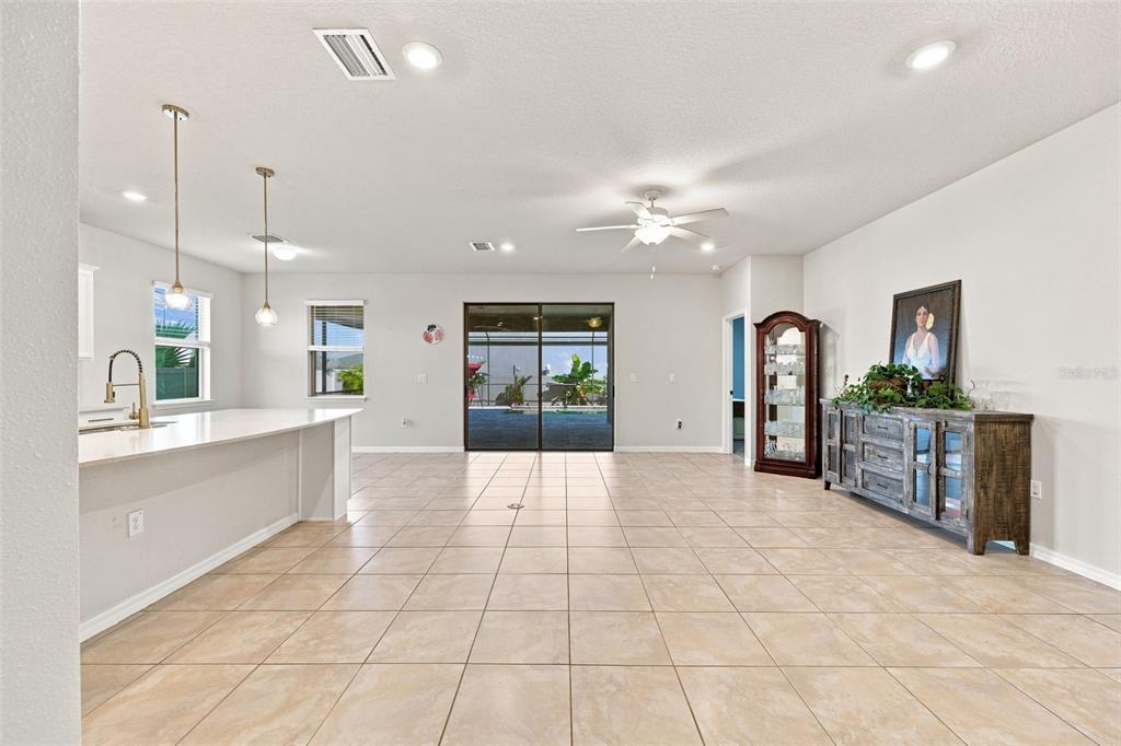 A bright, open-concept living area features light tile flooring, a kitchen island, and sliding glass doors — 18359 CORTES CREEK BOULEVARD, SPRING HILL, FL