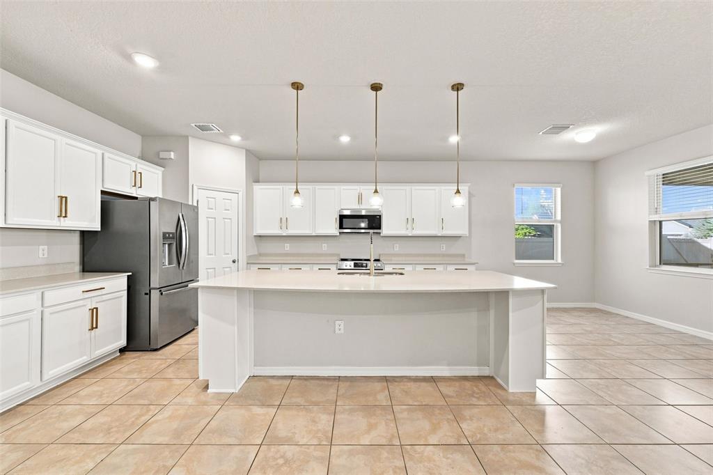A kitchen features white cabinets, a large island, stainless steel appliances, and tile flooring — 18359 CORTES CREEK BOULEVARD, SPRING HILL, FL