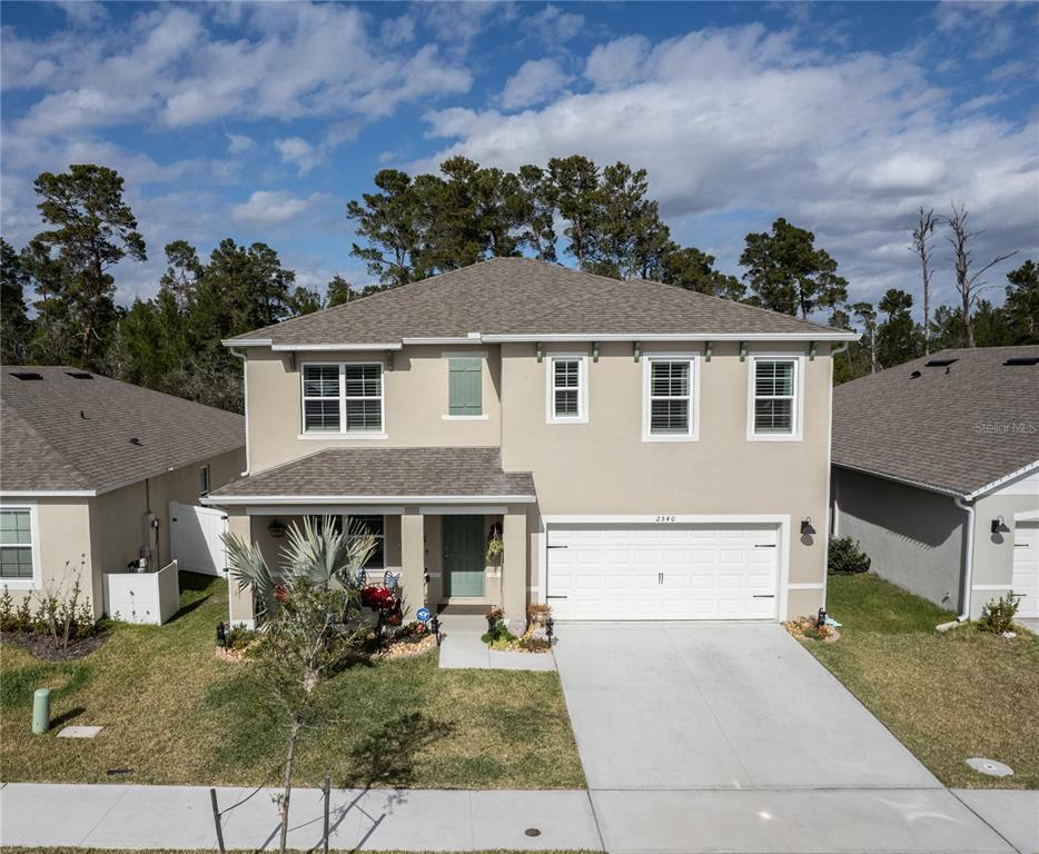 A two-story suburban house with a tan stucco exterior, a two-car garage, and a driveway — 2540 HARMONIA HAMMOCK ROAD, HARMONY, FL