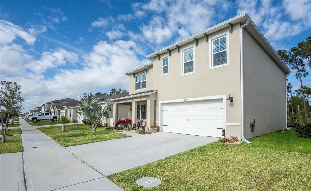 A two-story suburban house with a beige stucco exterior, white garage door, and concrete driveway — 2540 HARMONIA HAMMOCK ROAD, HARMONY, FL