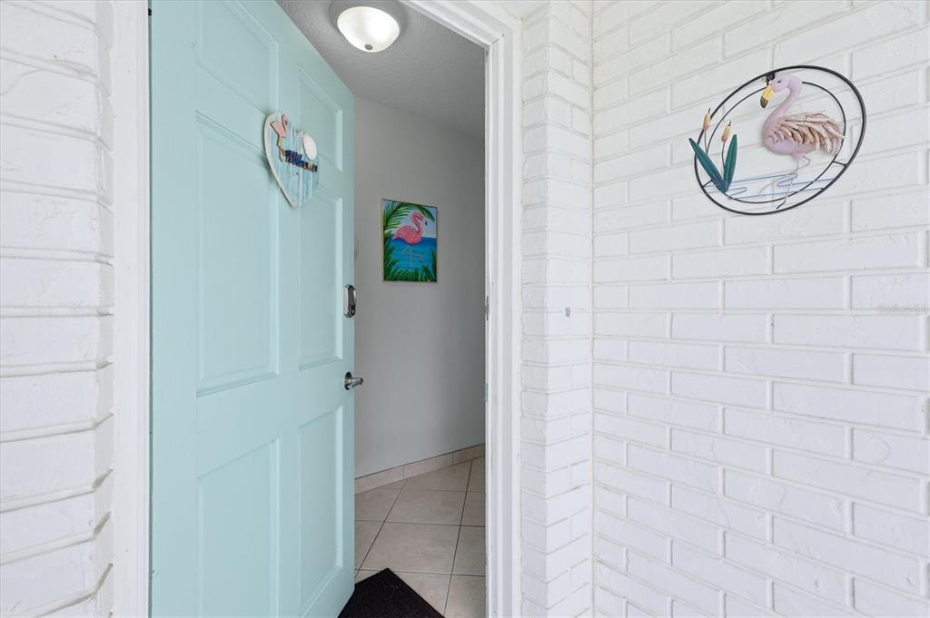 A light blue door opens into a tiled entryway featuring flamingo-themed wall decor — 6309 FLAMINGO DRIVE, APOLLO BEACH, FL