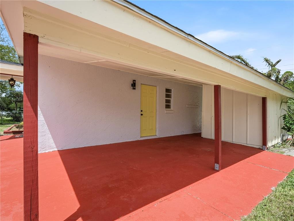 A covered carport with a red concrete floor and a yellow door on a house — 629 CEDAR PARK DRIVE, DAYTONA BEACH, FL