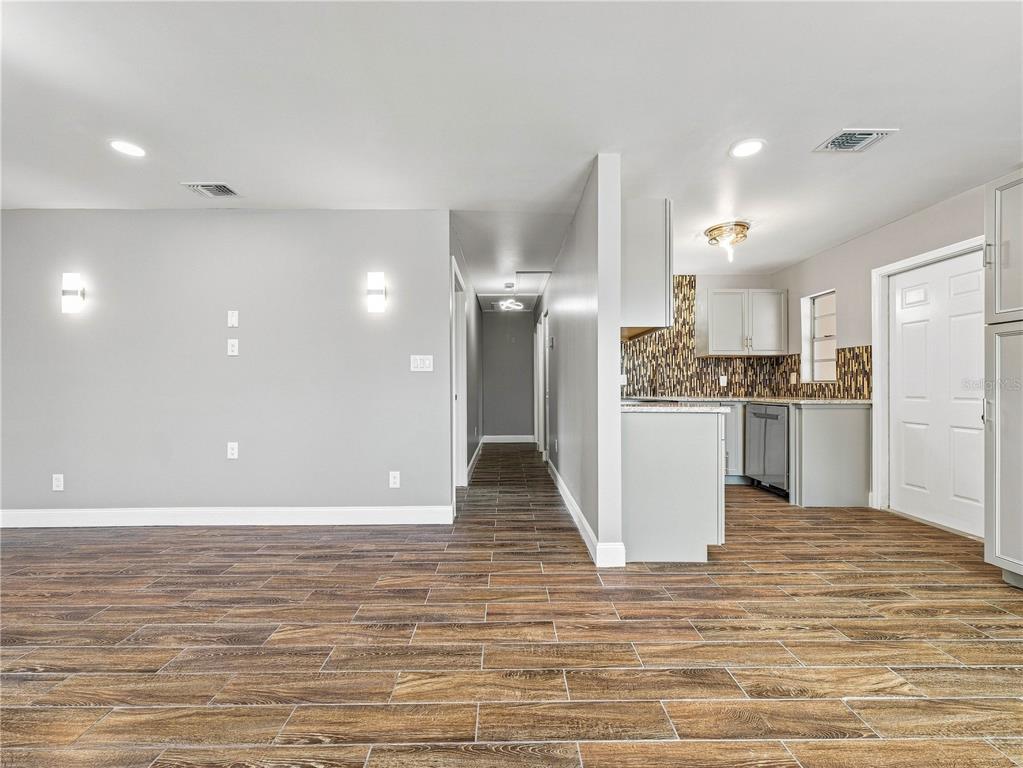A view of a living area with wood-look tile flooring leading into a small kitchen — 629 CEDAR PARK DRIVE, DAYTONA BEACH, FL