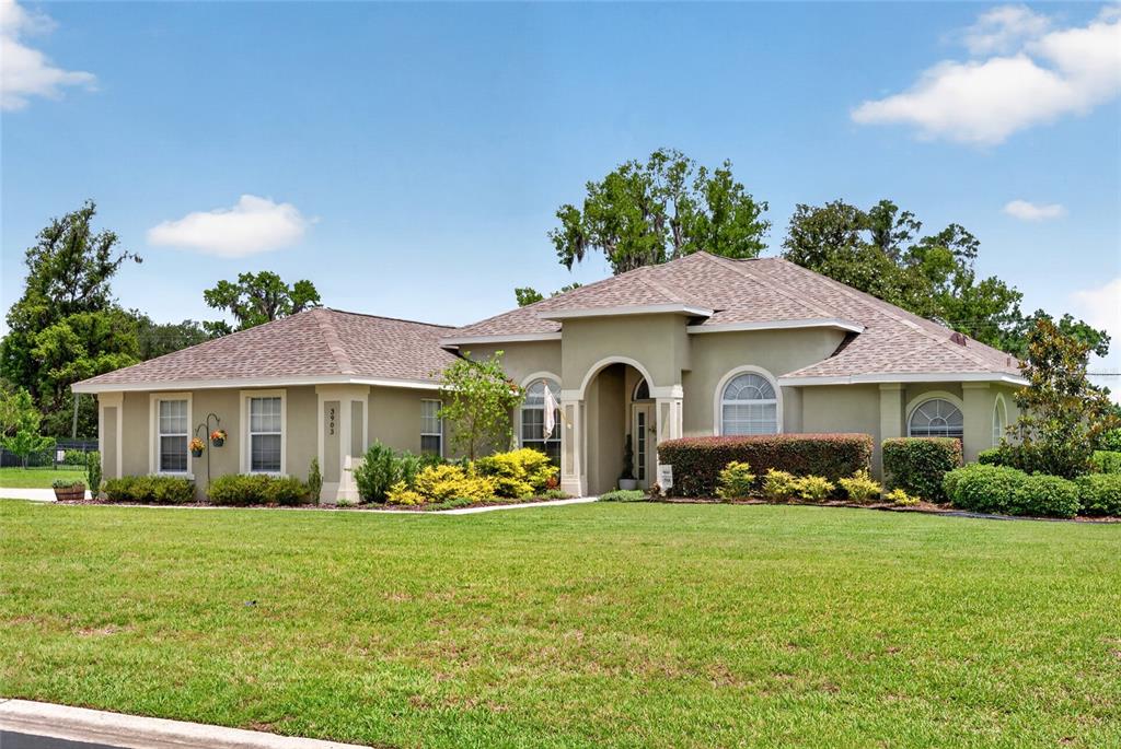 A single-story house with a tan stucco exterior, arched entryway, and a large front lawn — 3903 SE 38TH LOOP, OCALA, FL