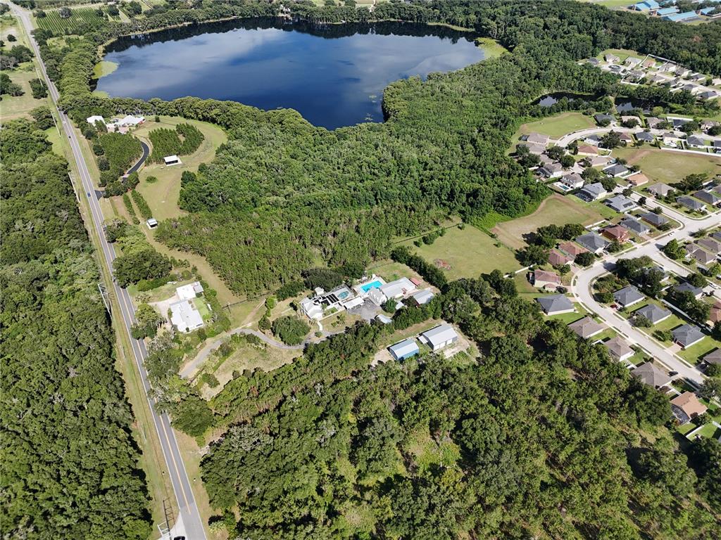 An aerial view shows a house with a pool, outbuildings, and forest near a lake — 00 E COUNTY ROAD 44, EUSTIS, FL